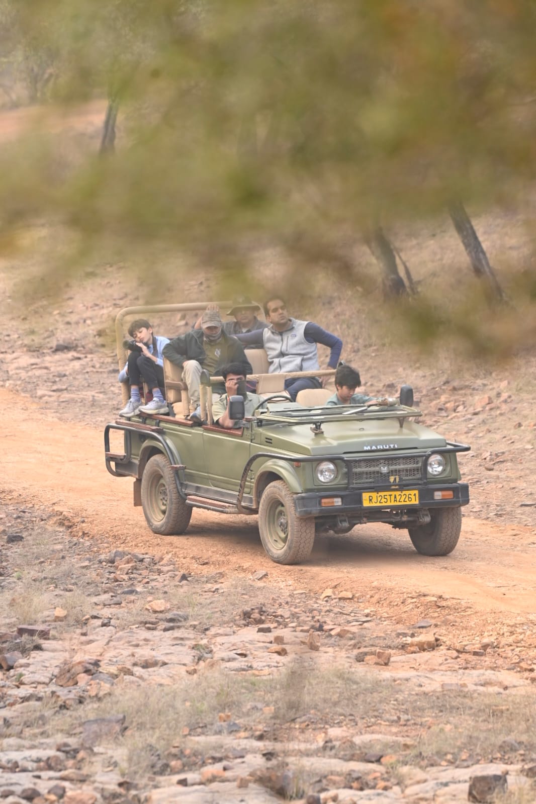 Maruti Gypsy 4x4 safari vehicle moving along a rocky trail through sparse dry forest inside Ranthambore